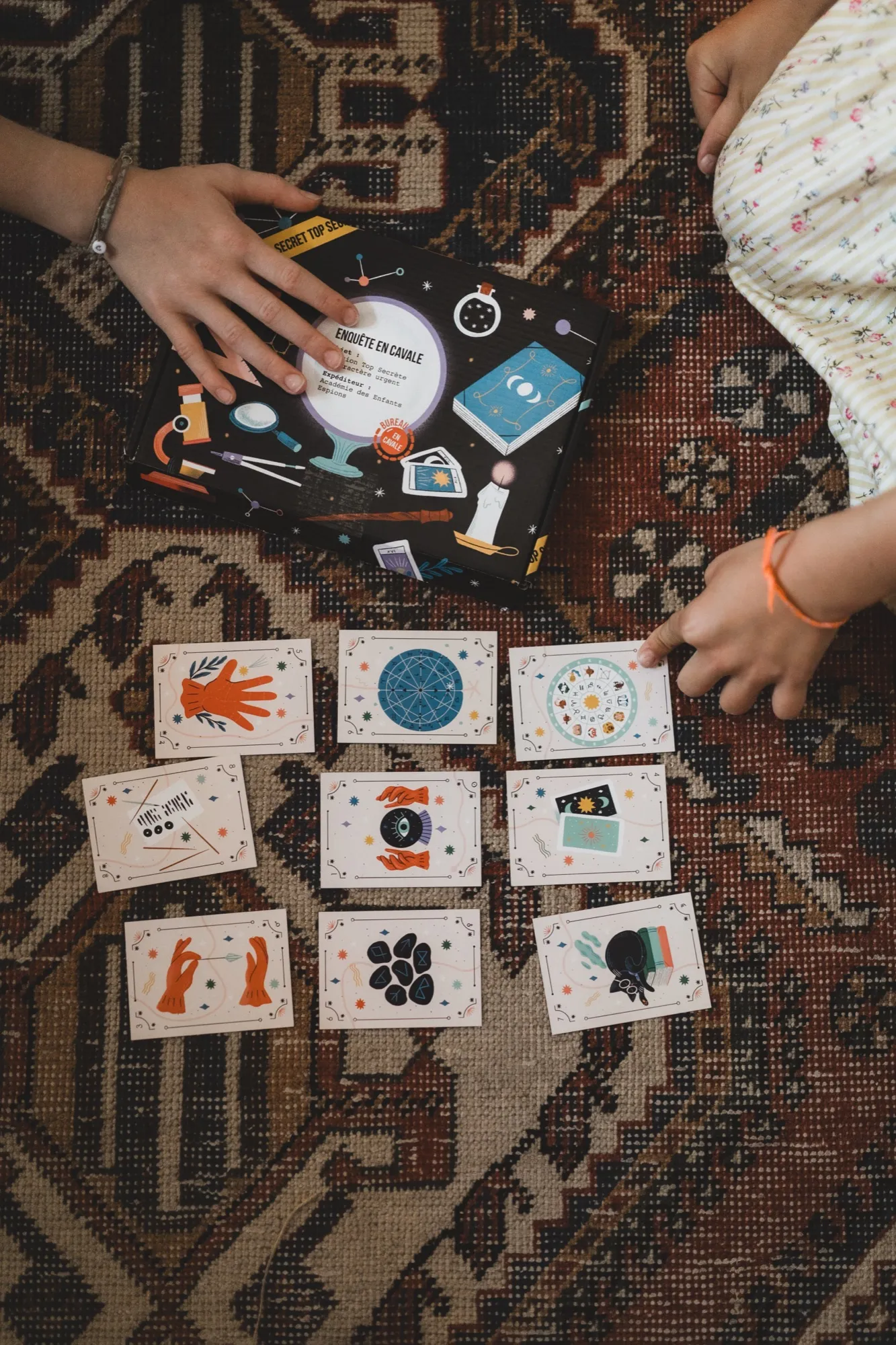 Enfants jouant avec une boîte En Cavale et ses cartes illustrées posées sur un tapis